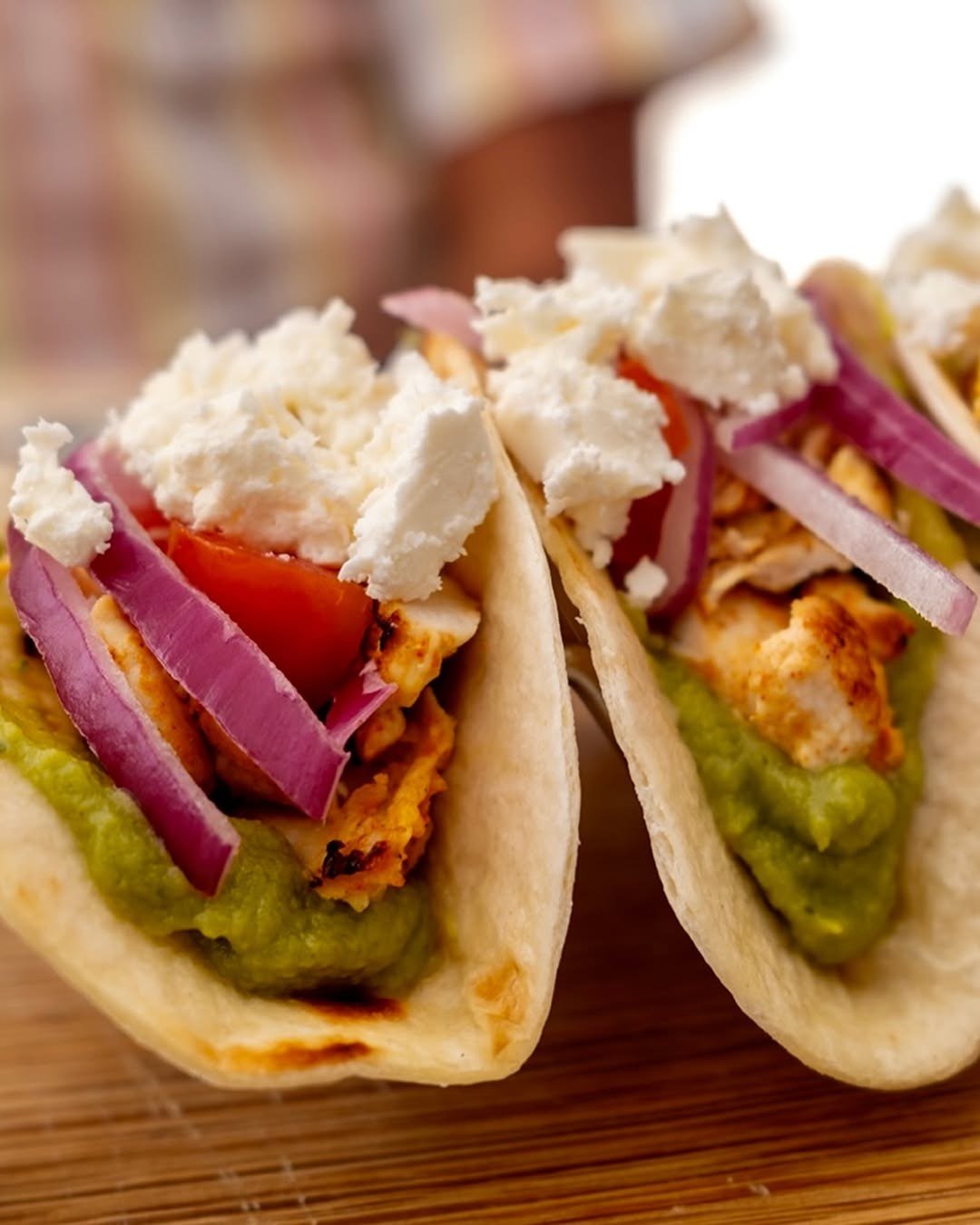 Dois tacos com guacamole, queijo branco, tomate e cebola roxa